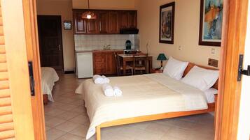 Une chambre d’hôtel comprenant un lit, un bureau, une chaise, une petite kitchenette et une porte donnant sur une autre pièce.