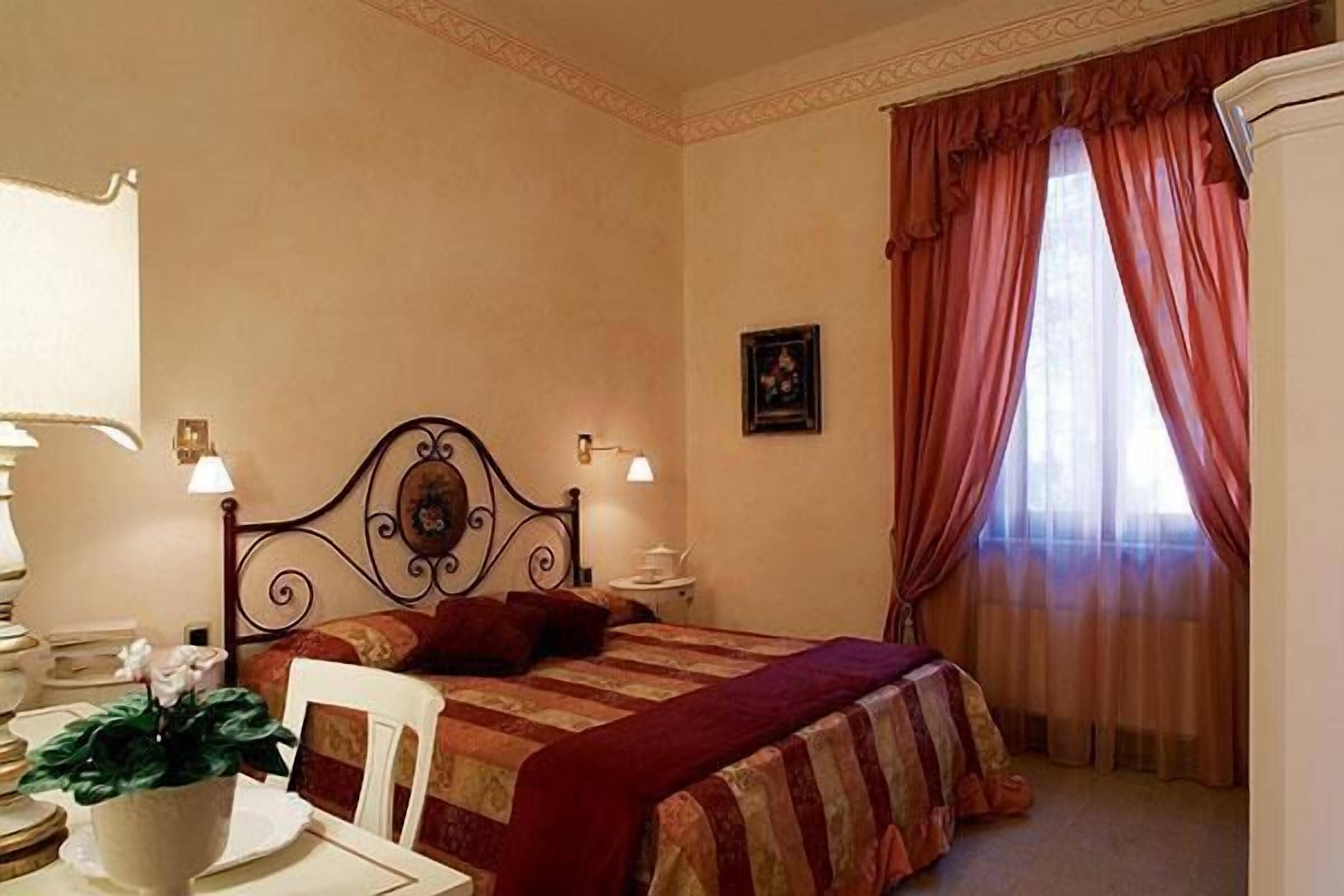 Ein Hotelzimmer mit Bett, Sessel, Schreibtisch mit Lampe und Fenster mit Vorhängen.