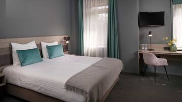 A neatly arranged hotel room with a large bed, a desk, a chair, a TV, and a window with curtains.