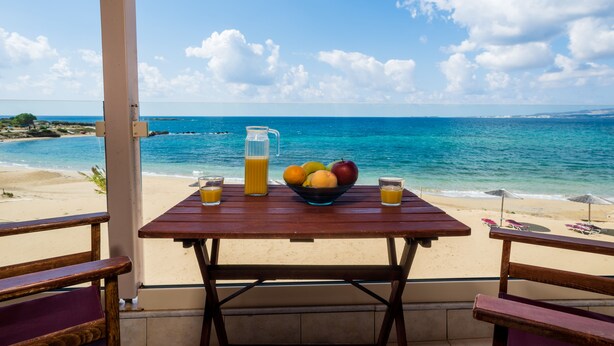 Una taula de fusta amb un plat de fruita i begudes, amb vista a una platja i l'oceà.