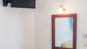 Habitació amb escriptori de fusta, mirall, televisió penjada a la paret i una petita banca amb funda floral.