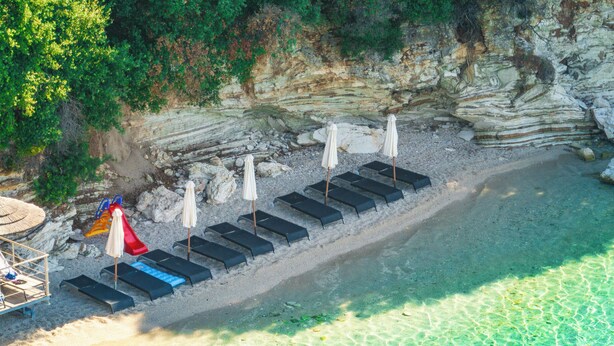 A beach with sun loungers and umbrellas, clear water, and rocky cliffs. - San Nicolas Resort Hotel (Lefkada)