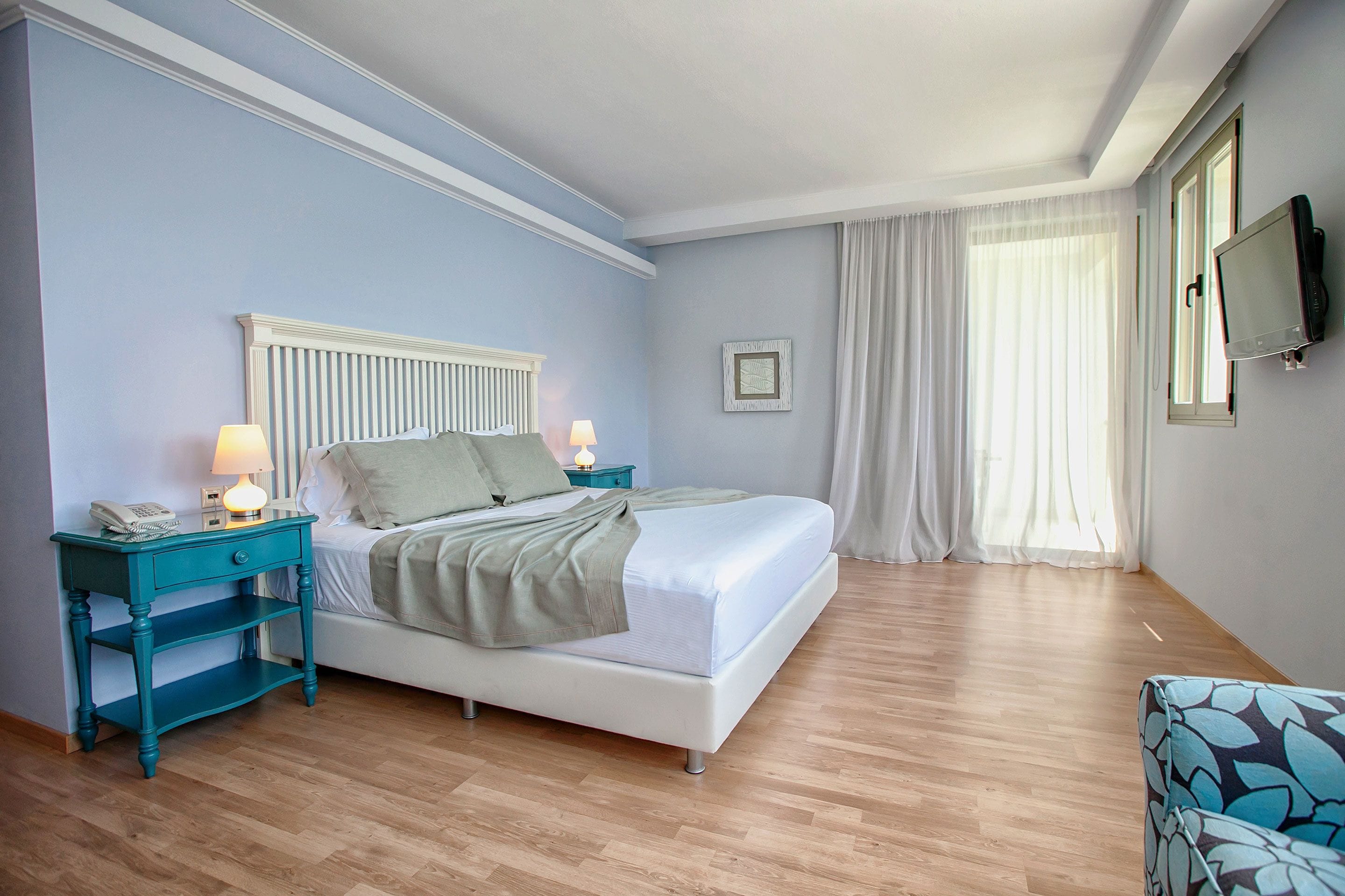 Una camera da letto con un letto, comodini, una televisione e una finestra con tende.