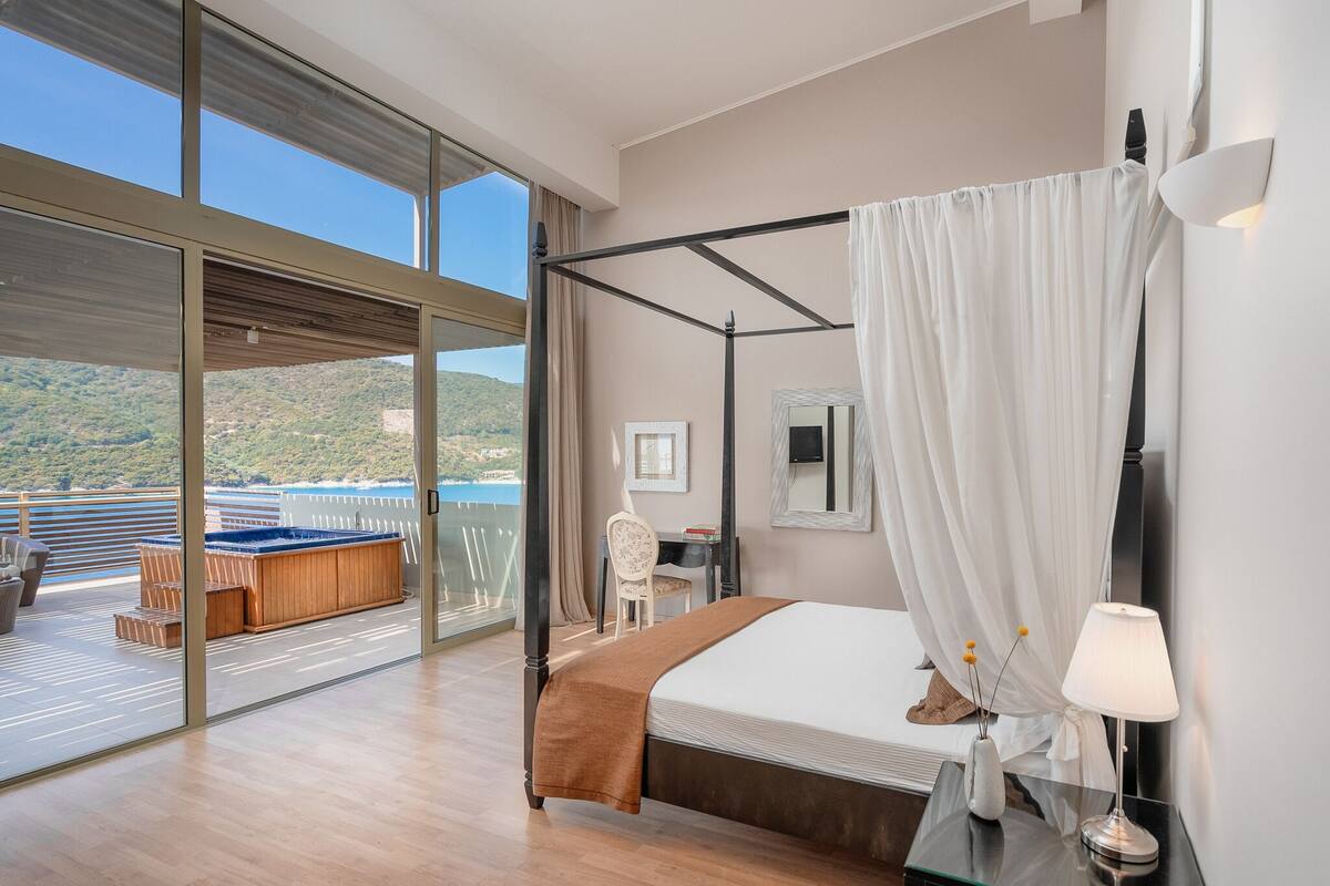 Un dormitorio moderno con una cama grande, un ventanal que da a un balcón con hidromasaje y vistas al mar.
