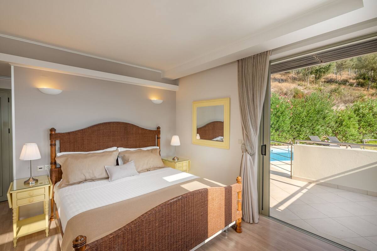 Un dormitorio con una cama grande, mesitas de noche, un espejo y vistas a una piscina y zonas verdes.