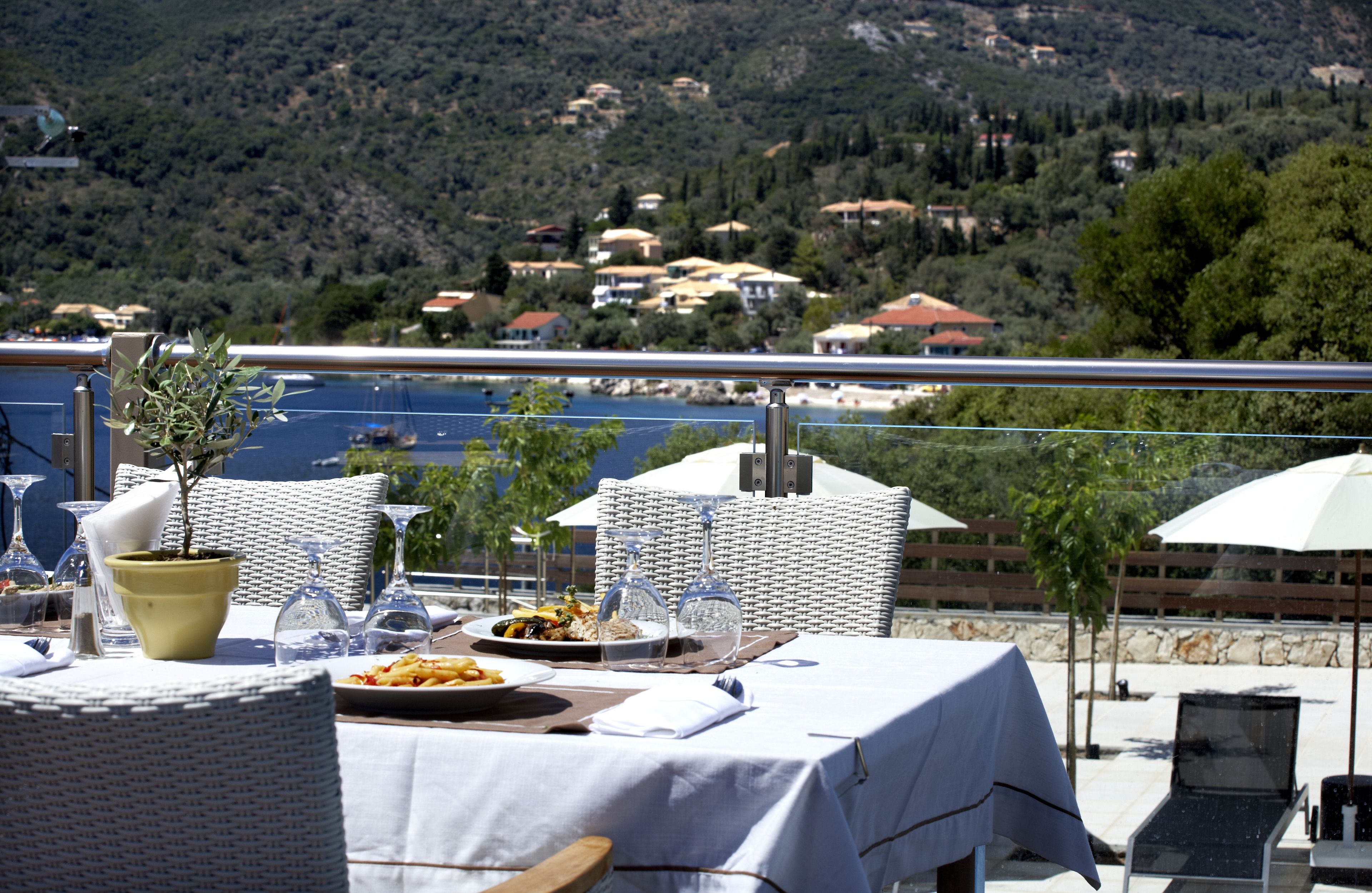 A dining area with a table set for two, overlooking a scenic hillside with houses.