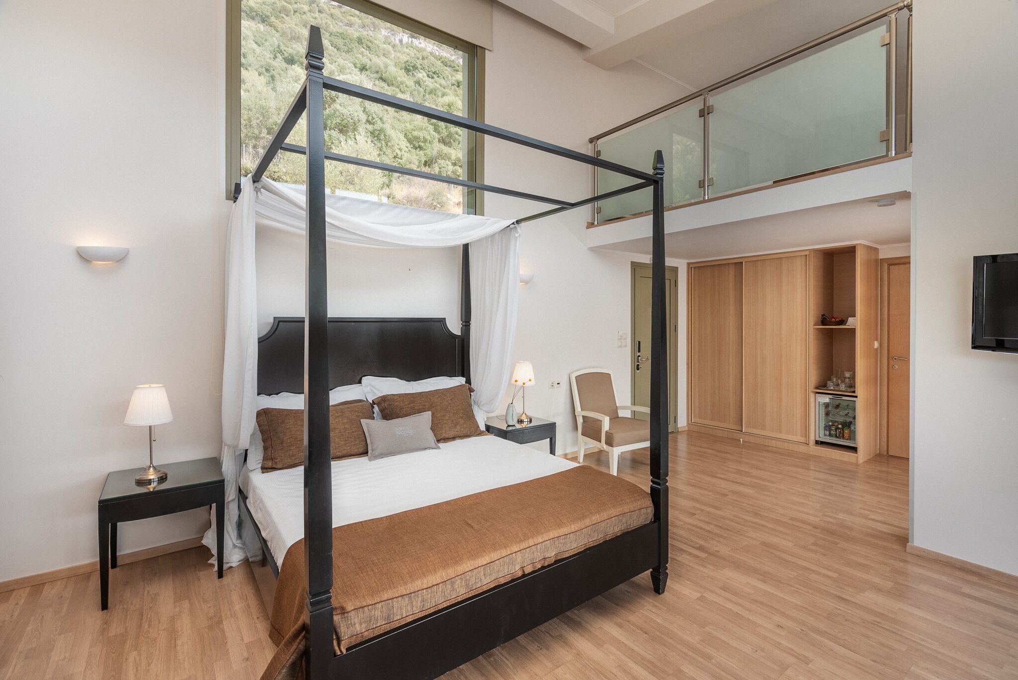 A modern bedroom with a four-poster bed, a nightstand with a lamp, a chair, and a wardrobe.