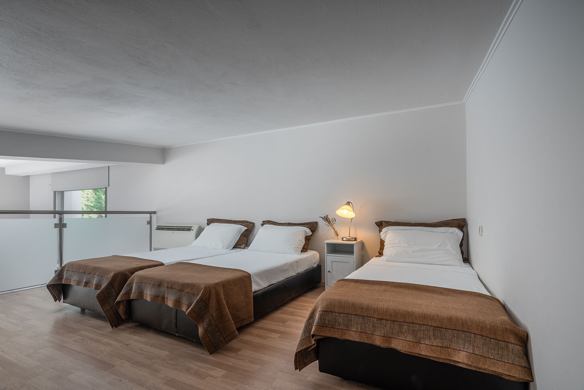 Une chambre d’hôtel moderne avec trois lits, un balcon et une grande fenêtre.