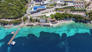 An aerial view of a coastal hotel with multiple buildings, a dock, and clear turquoise waters. - San Nicolas Resort Hotel (Lefkada)