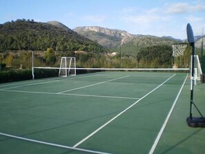 An outdoor tennis court with a net, goalpost, and a basketball hoop. - loftOtel canet (Esporles)