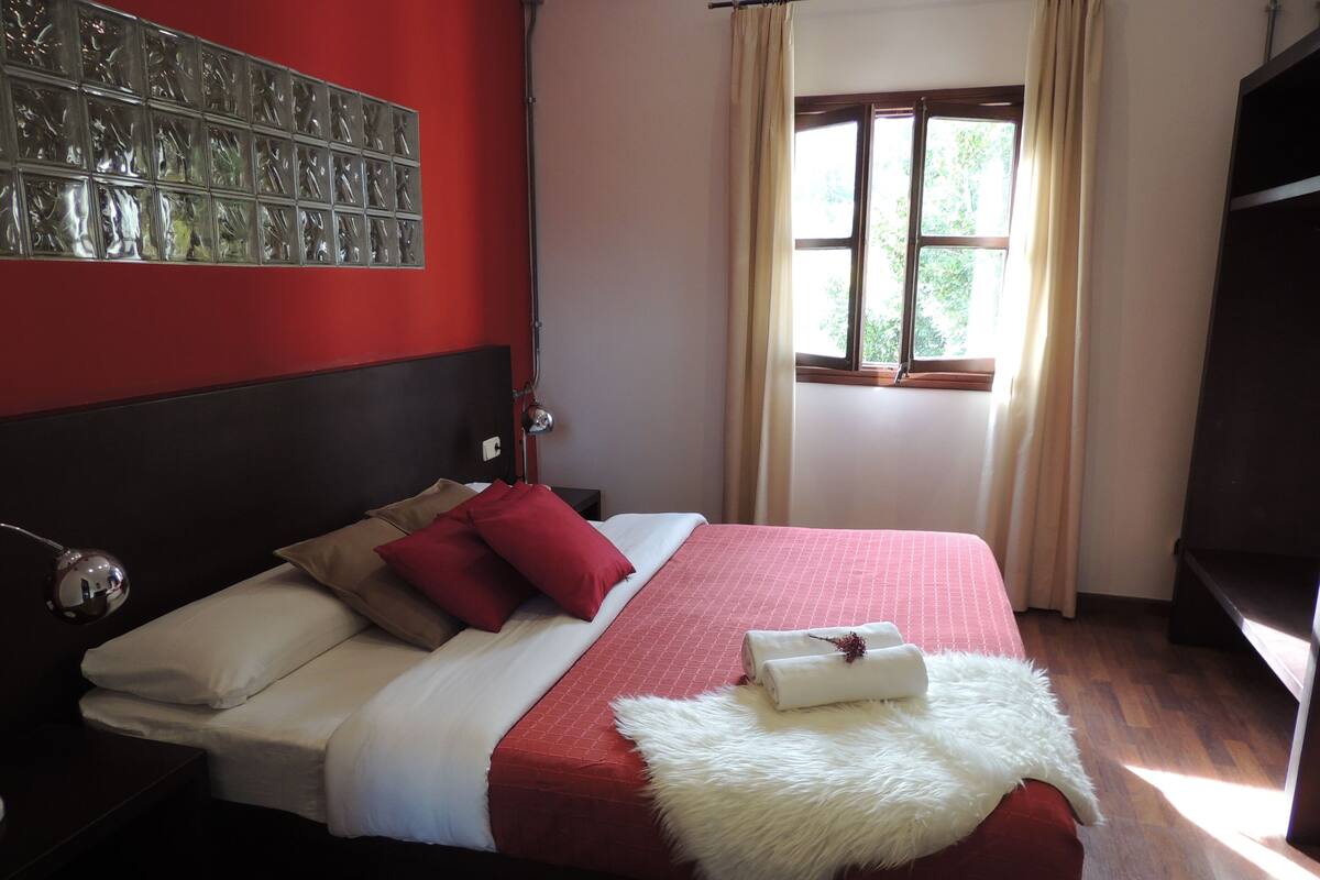 Una cama bien tendida con colcha roja y blanca, un suave plaid blanco y una disposición de almohadas rojas y marrones.