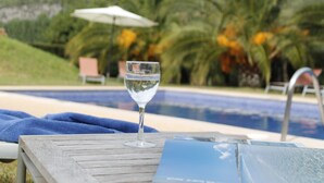 A glass of water on a wooden table with a brochure, near a pool with a chair and umbrella in the background. - loftOtel canet (Esporles)