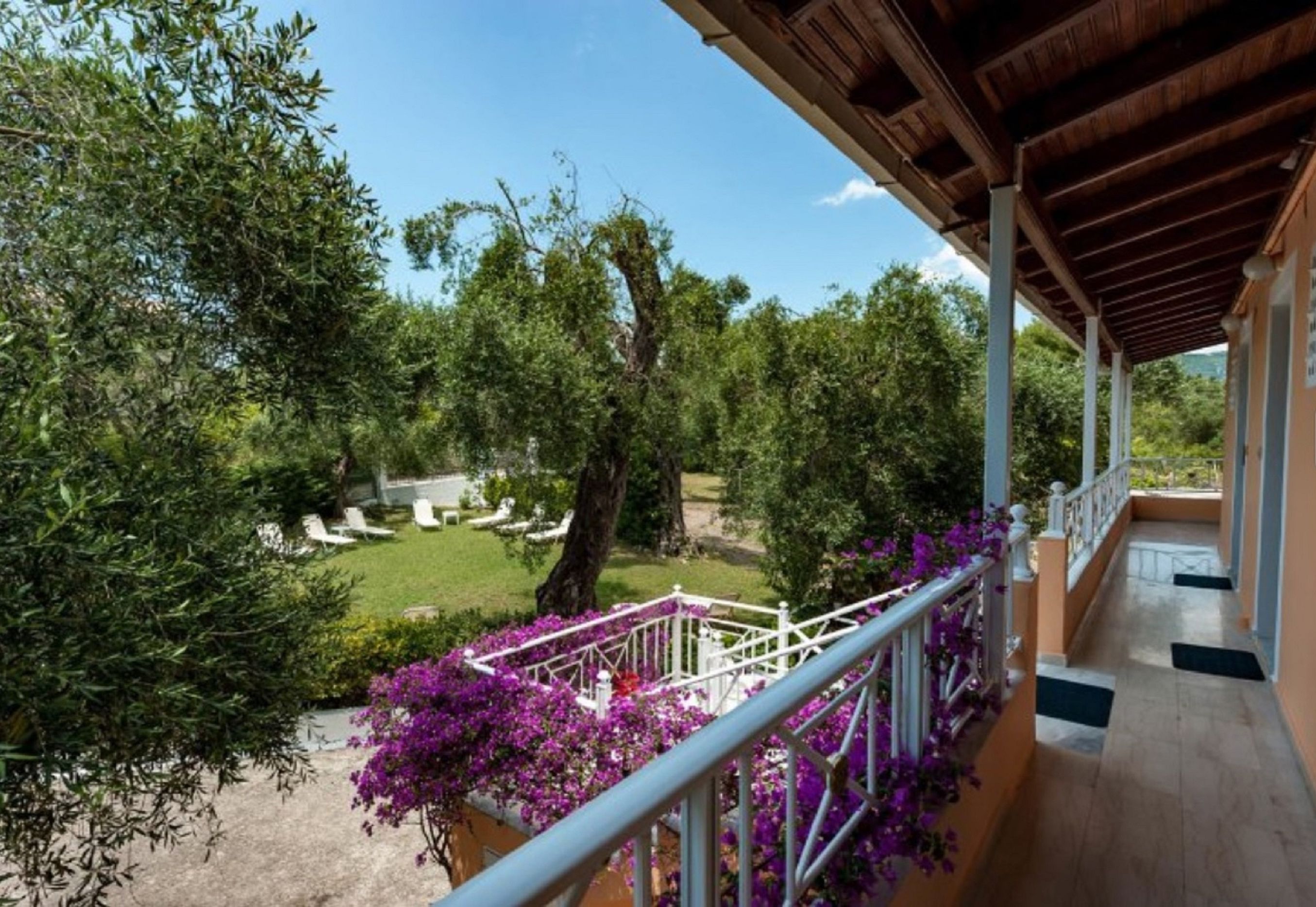 A balcony with a view of a garden, a wooden pergola, and a white railing.