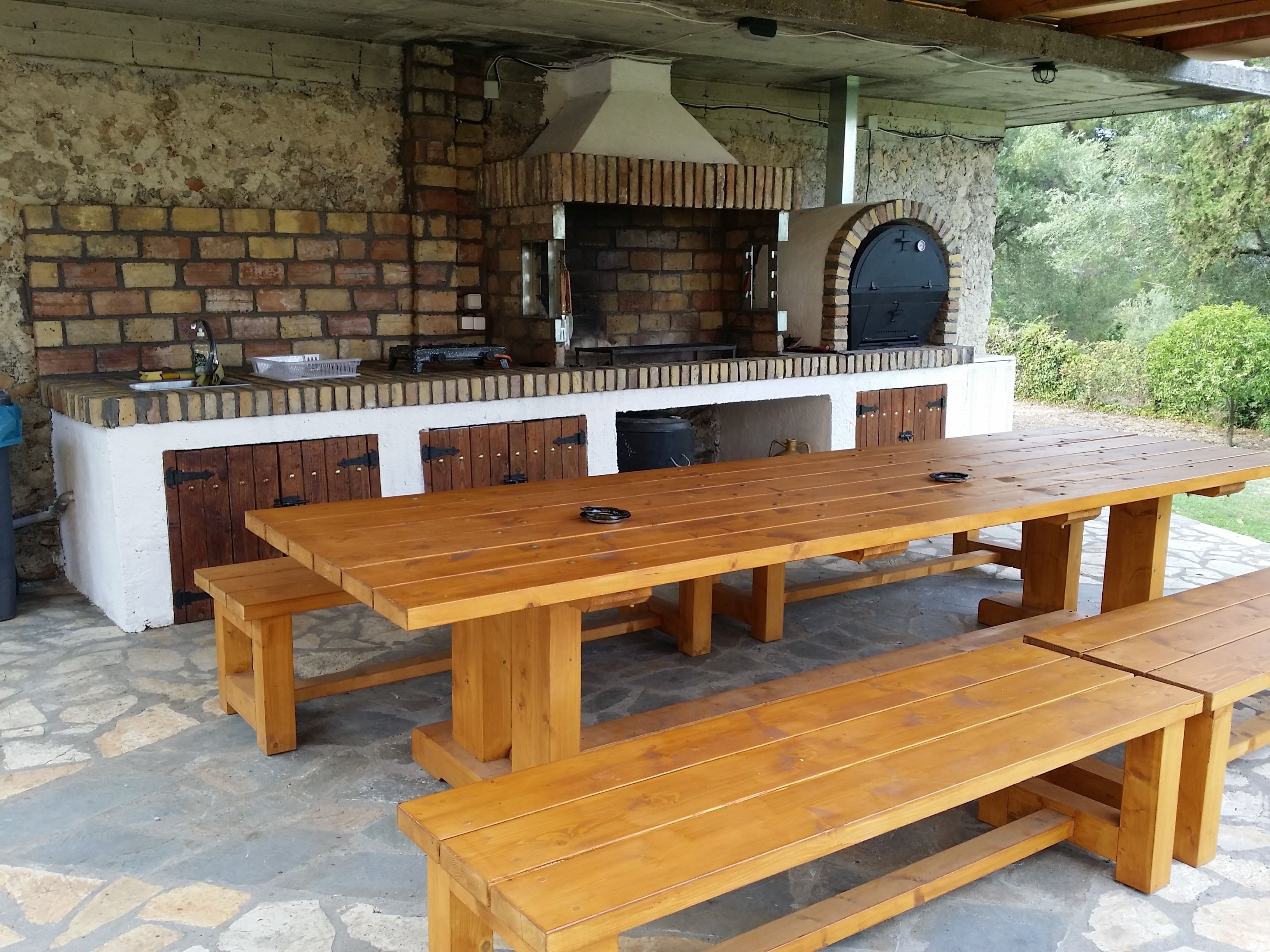 An outdoor kitchen with a brick wall, a large oven, and a wooden table with benches.