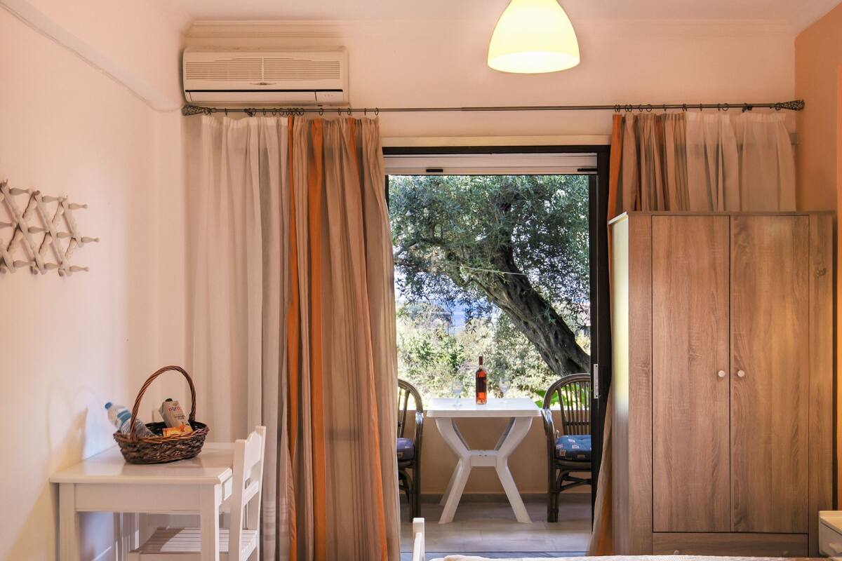 A bedroom with two beds, a table with a chair, a wardrobe, and a view of the outdoors.