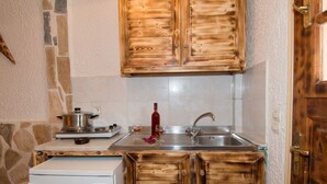 A compact kitchen with wooden cabinets, a white refrigerator, a stove, and a sink. - Lofos Studios (Zakynthos)