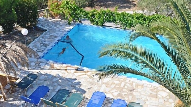 A swimming pool with a stone border, surrounded by lounge chairs and palm trees. - Lofos Studios (Zakynthos)