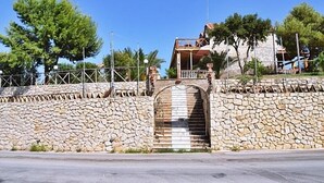 A stone wall with a metal gate, a staircase leading to a building with a balcony, and a clear blue sky. - Lofos Studios (Zakynthos)