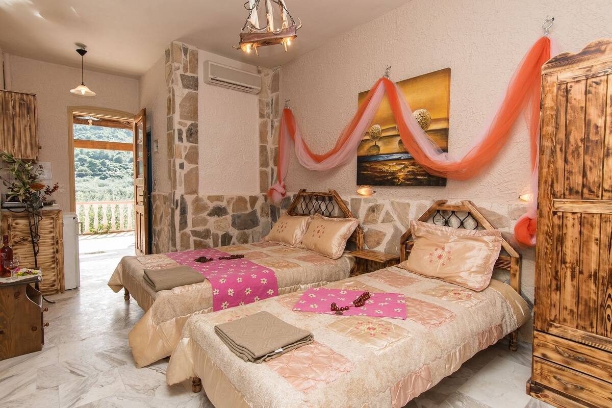 A bedroom with two beds, a stone wall, a wooden cabinet, and a painting.