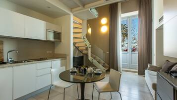 A compact kitchen with a modern design, a dining area with a glass table, and a staircase leading to a balcony with a view.