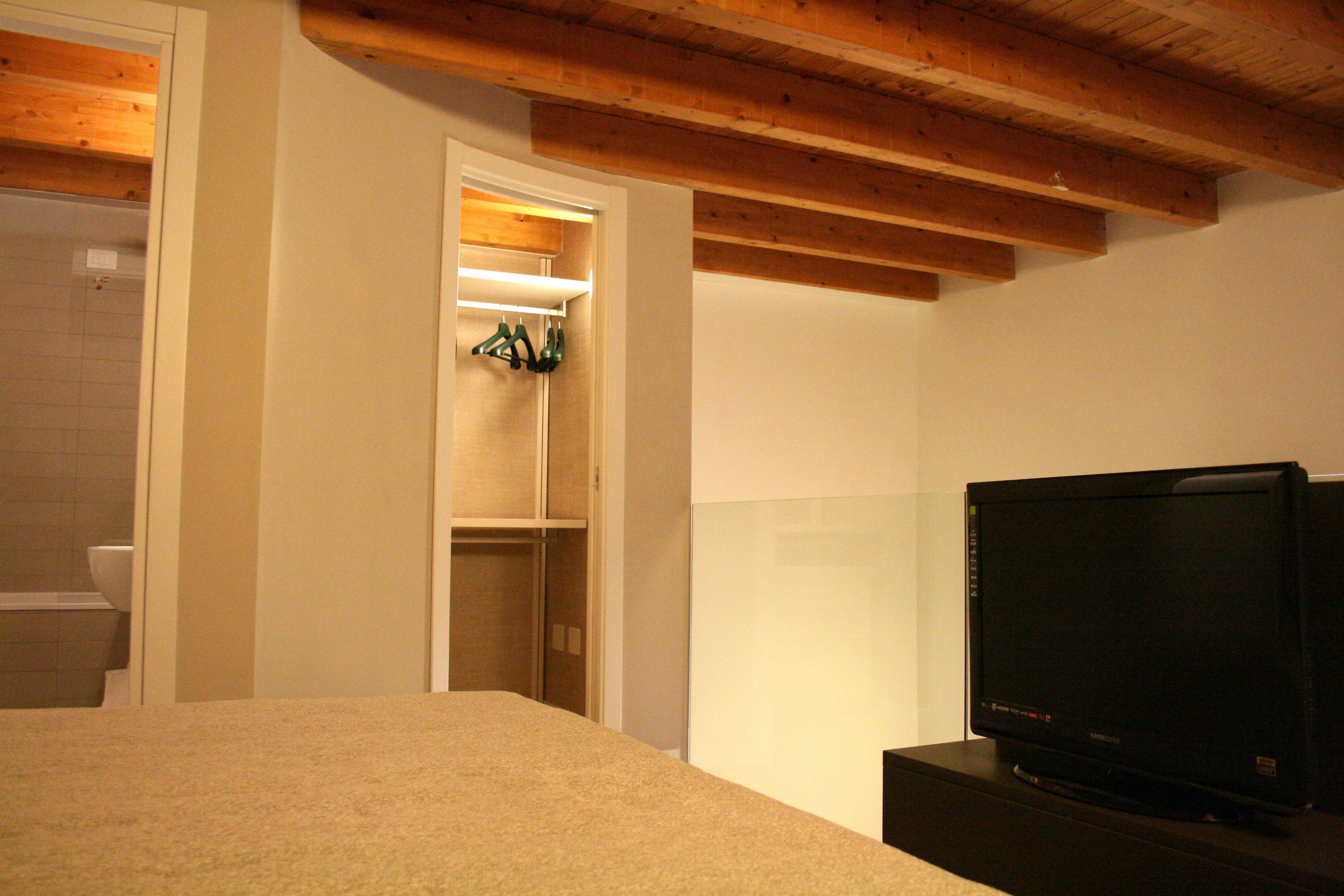 A bedroom with a bed, a television, and a closet with hanging clothes.