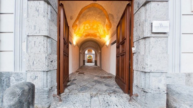A stone corridor with wooden doors and a stone floor, leading to a central archway. - Villa Avellino (Pozzuoli)