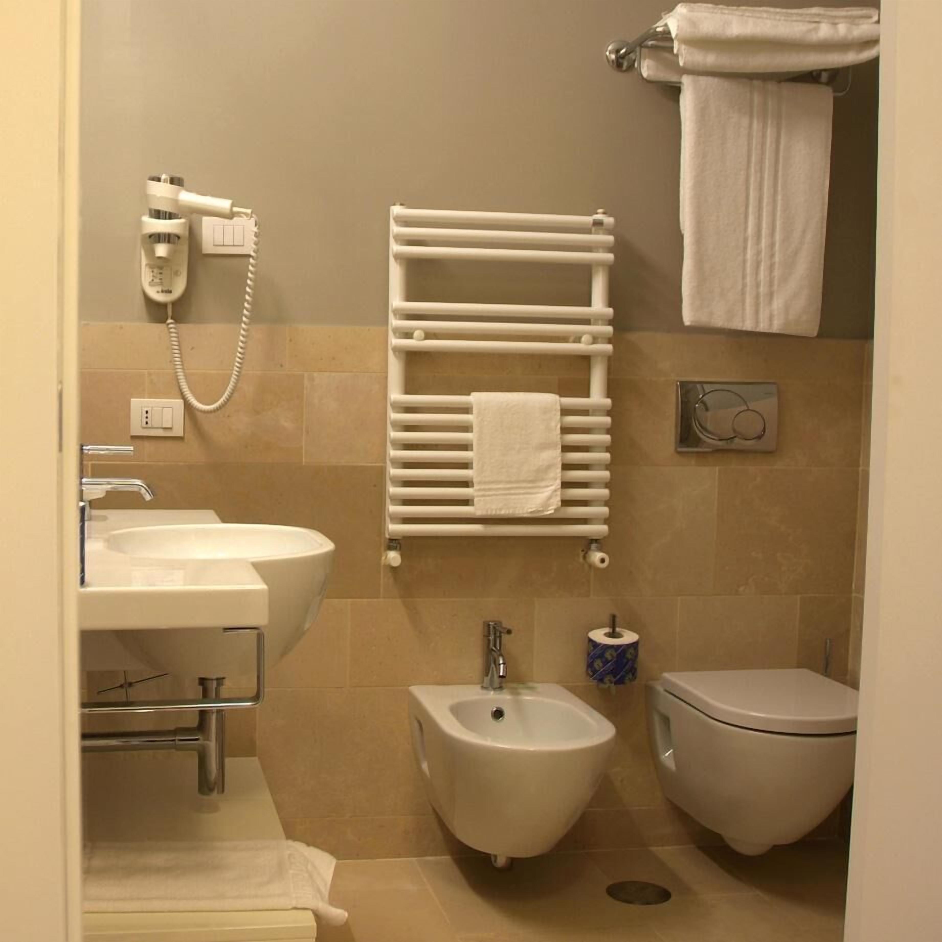 A bathroom with a sink, bidet, toilet, towel rack, and a telephone.