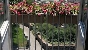 A balcony with pink flowers, a view of the sea, and buildings in the distance. - Villa Avellino (Pozzuoli)