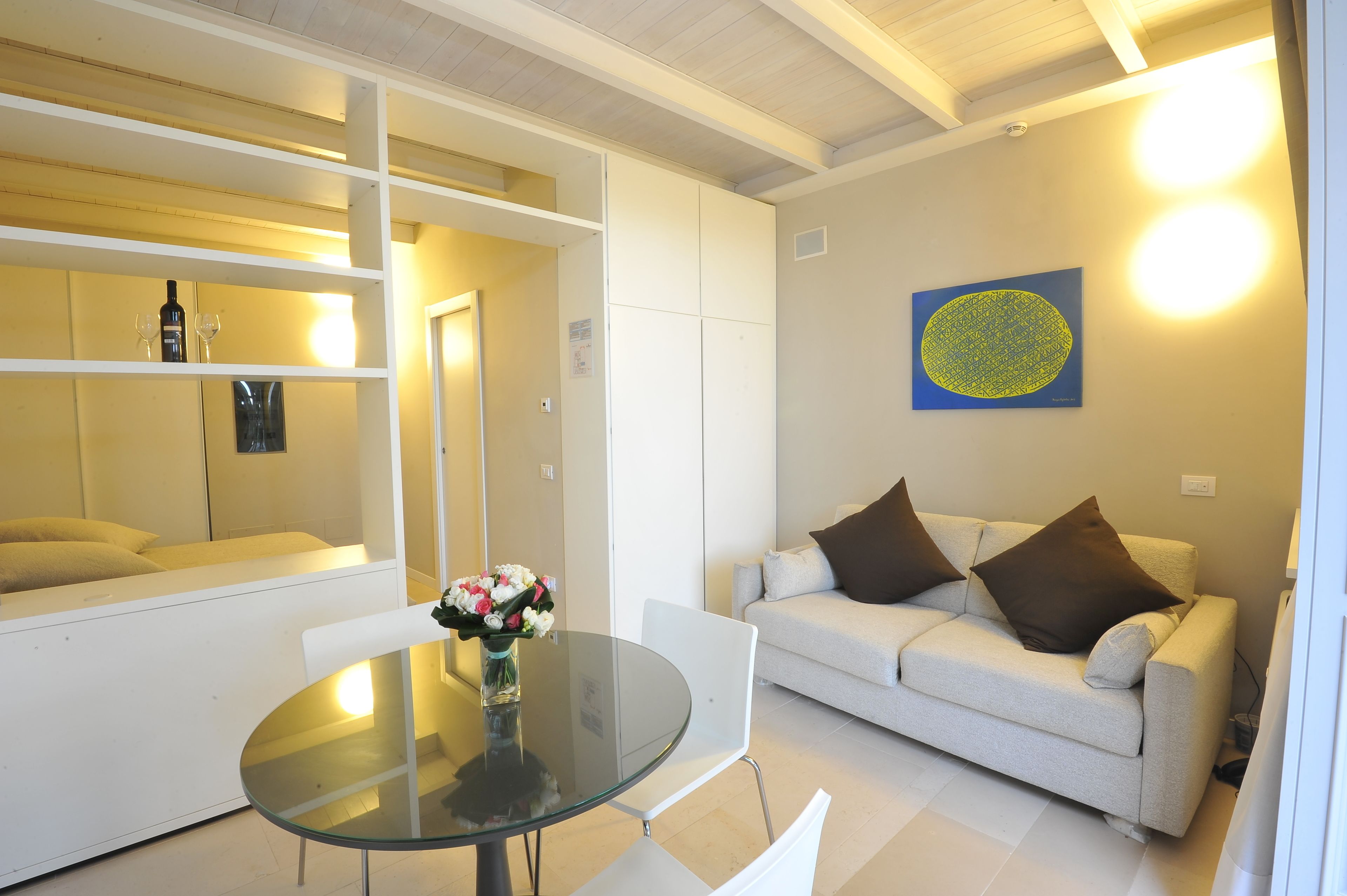Una sala de estar moderna con una mesa de comedor de cristal, un sofá y una obra de arte colgada en la pared.
