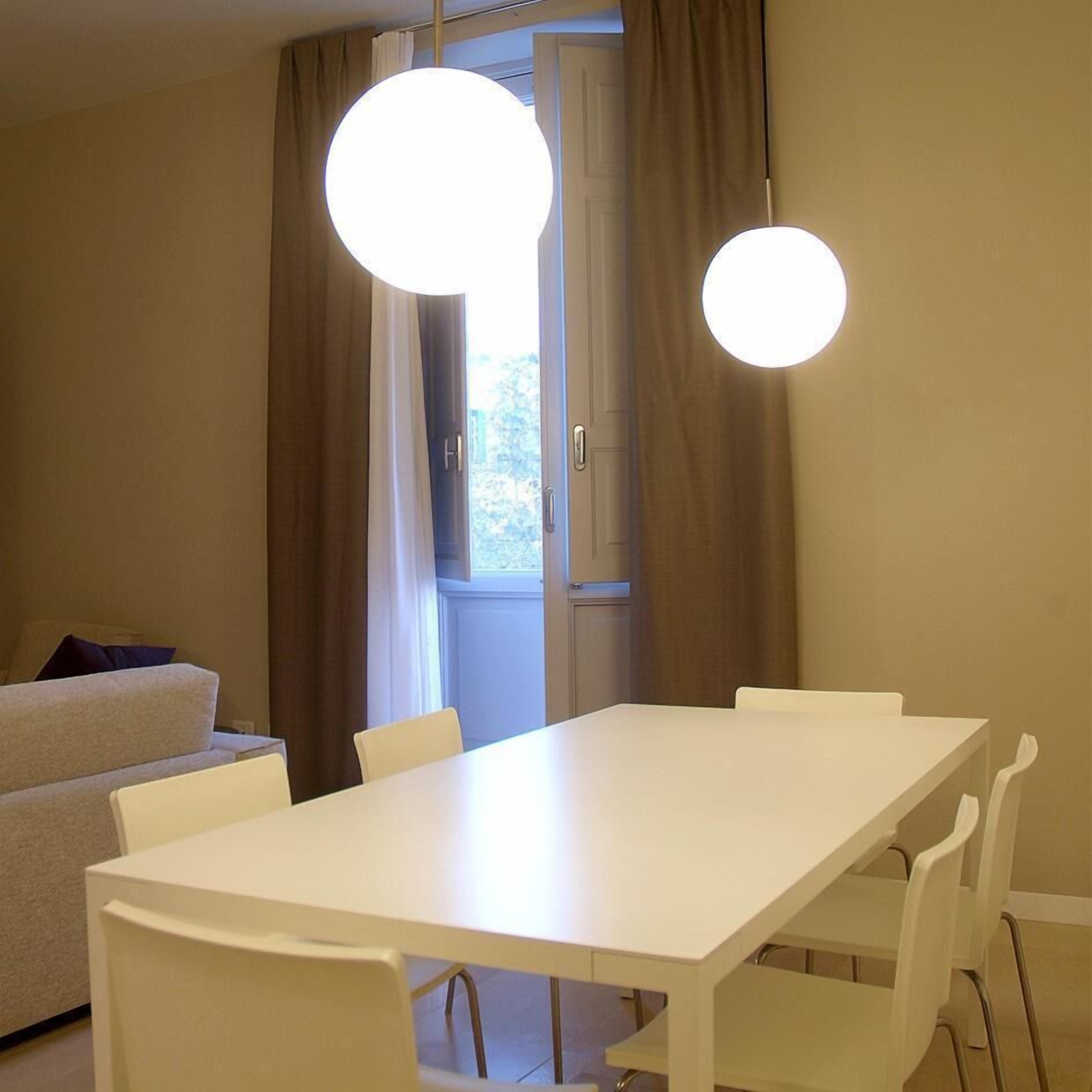 A modern dining area with a white table and chairs, a sofa in the background, and two pendant lights.