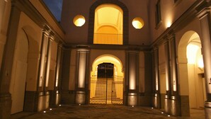 A courtyard with a central arched entrance, flanked by columns and illuminated by wall-mounted lights. - Villa Avellino (Pozzuoli)