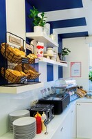 A breakfast buffet with labeled food items, a coffee station, and a plant on the wall.