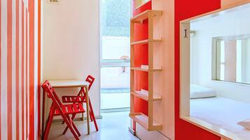 Une chambre d’hôtel moderne avec un lit blanc, un mur rayé de rouge et de blanc, une chaise rouge et une fenêtre donnant sur un beau paysage.