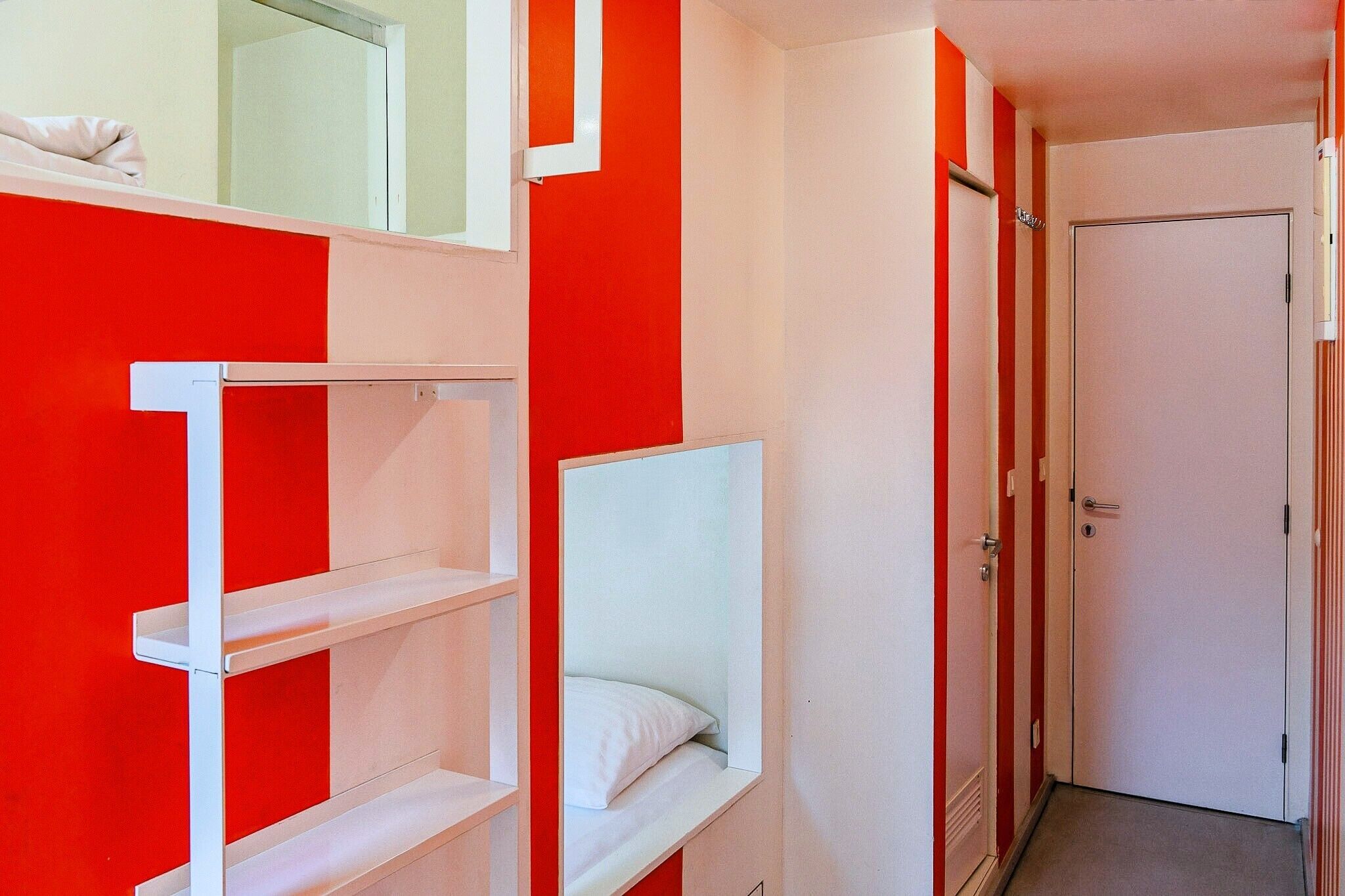 Une chambre avec un lit superposé, une porte blanche et des murs rouges.