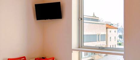 A hotel room with two beds, a TV mounted on the wall, and a window with a view of buildings.