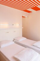 A hotel room with two beds, a ceiling with orange stripes, and wall-mounted lights.