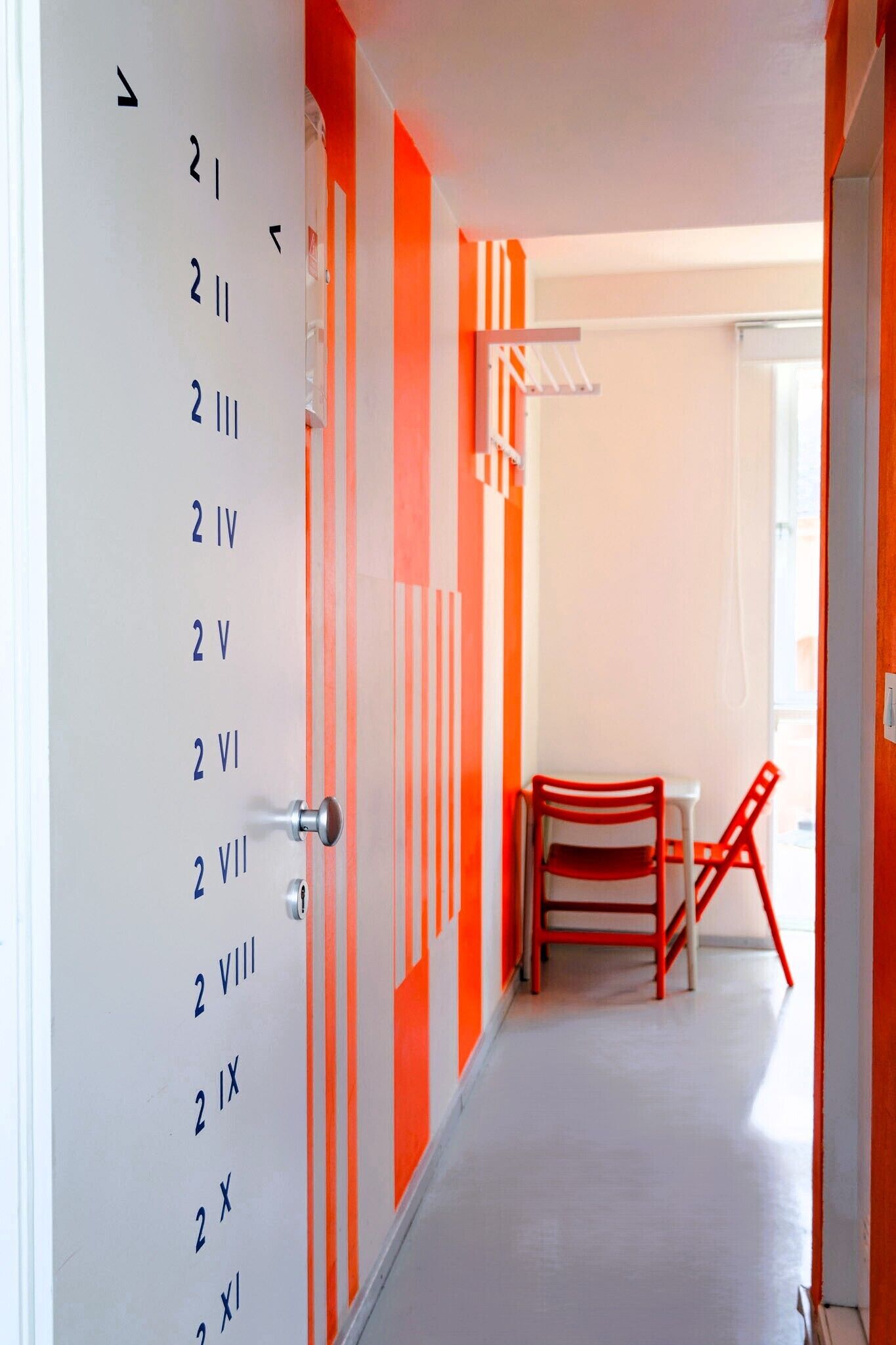 A hallway with numbered doors, a red chair, and a small table.