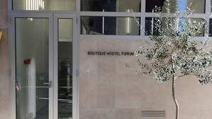 Egy épület, amelyen egy „BOUTIQUE HOSTEL FORUM” feliratú tábla látható, és előtte egy virágtartóban lévő fa áll.