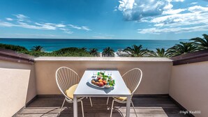 Ein Balkon mit Tisch für zwei Personen, Blick auf einen Strand mit klarem, blauem Wasser und Palmen.