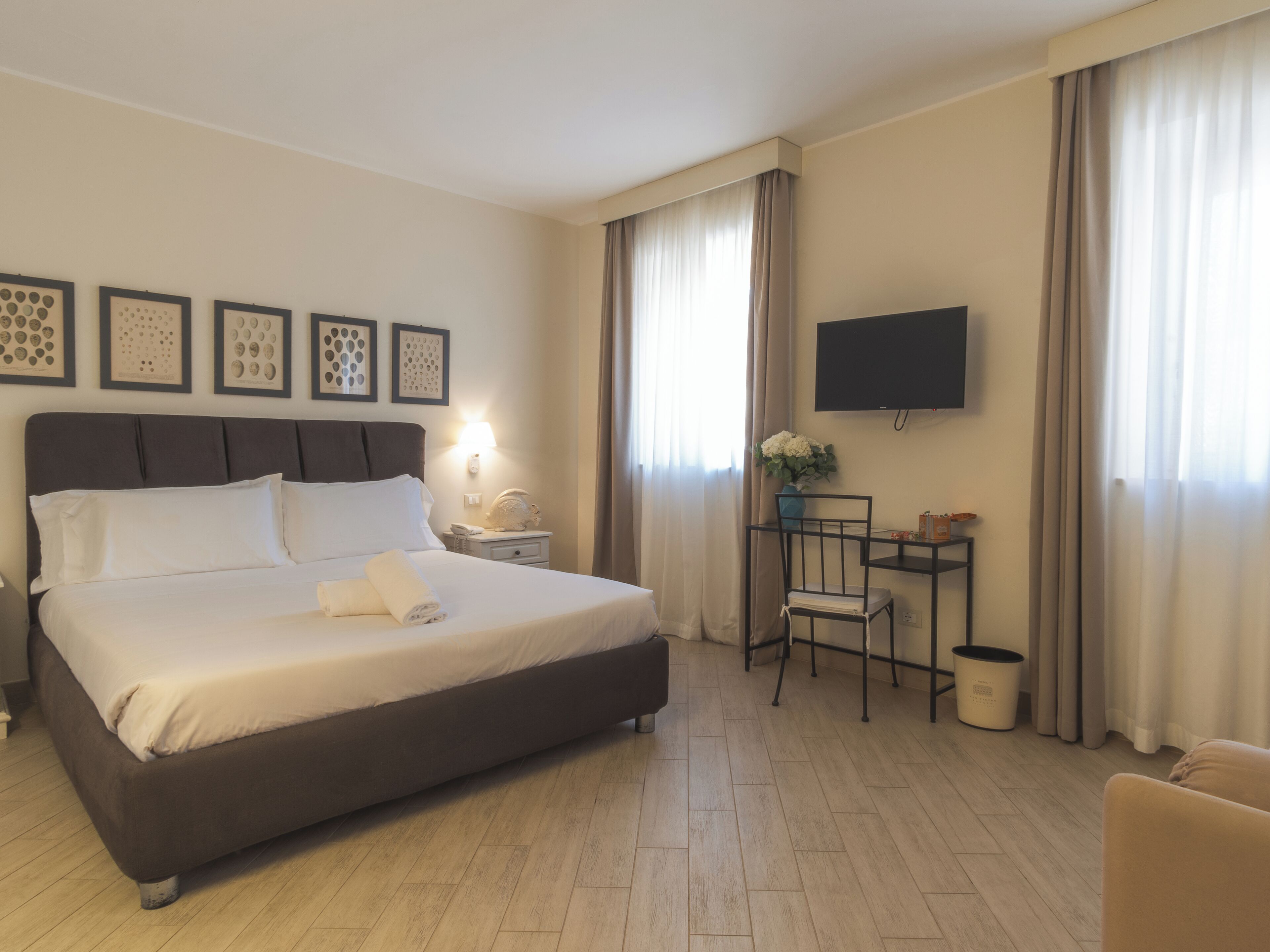 Una habitación de hotel con cama, escritorio, silla, televisor y cuadros en la pared.