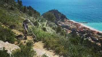 A mountain biker on a dirt trail with a coastal town in the background.