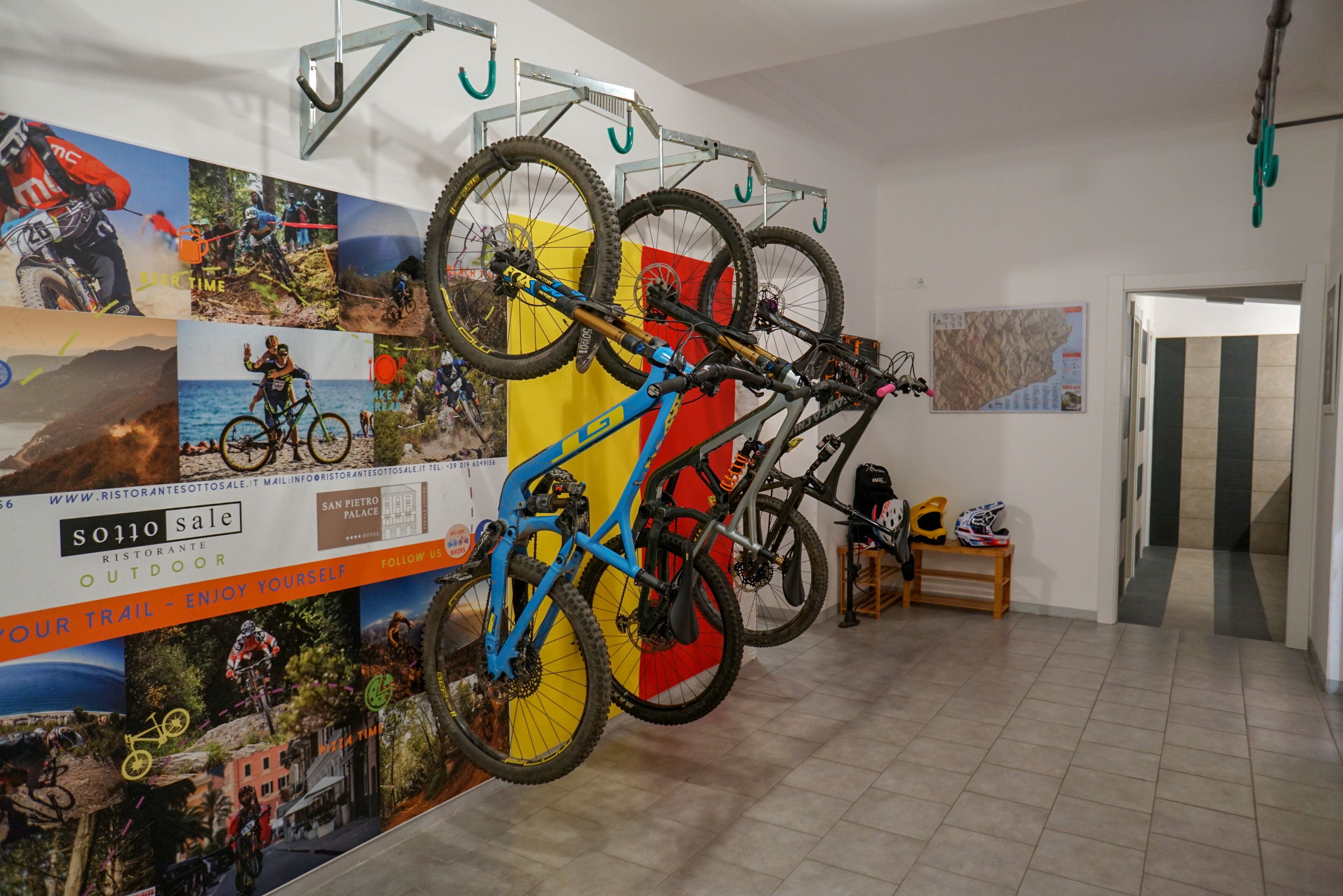 Ein Raum mit einem an der Wand befestigten Fahrradständer, der zwei Fahrräder trägt, einer Holzbank und einer Tür zu einem weiteren Bereich.
