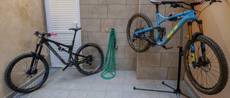 Un porte-vélos avec deux vélos, un tuyau d’arrosage vert et une porte blanche.
