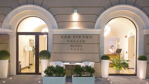 Das äußere Erscheinungsbild des San Pietro Palace Hotels mit einer Rezeption, zwei Kübelpflanzen und einem Schild über dem Eingang.