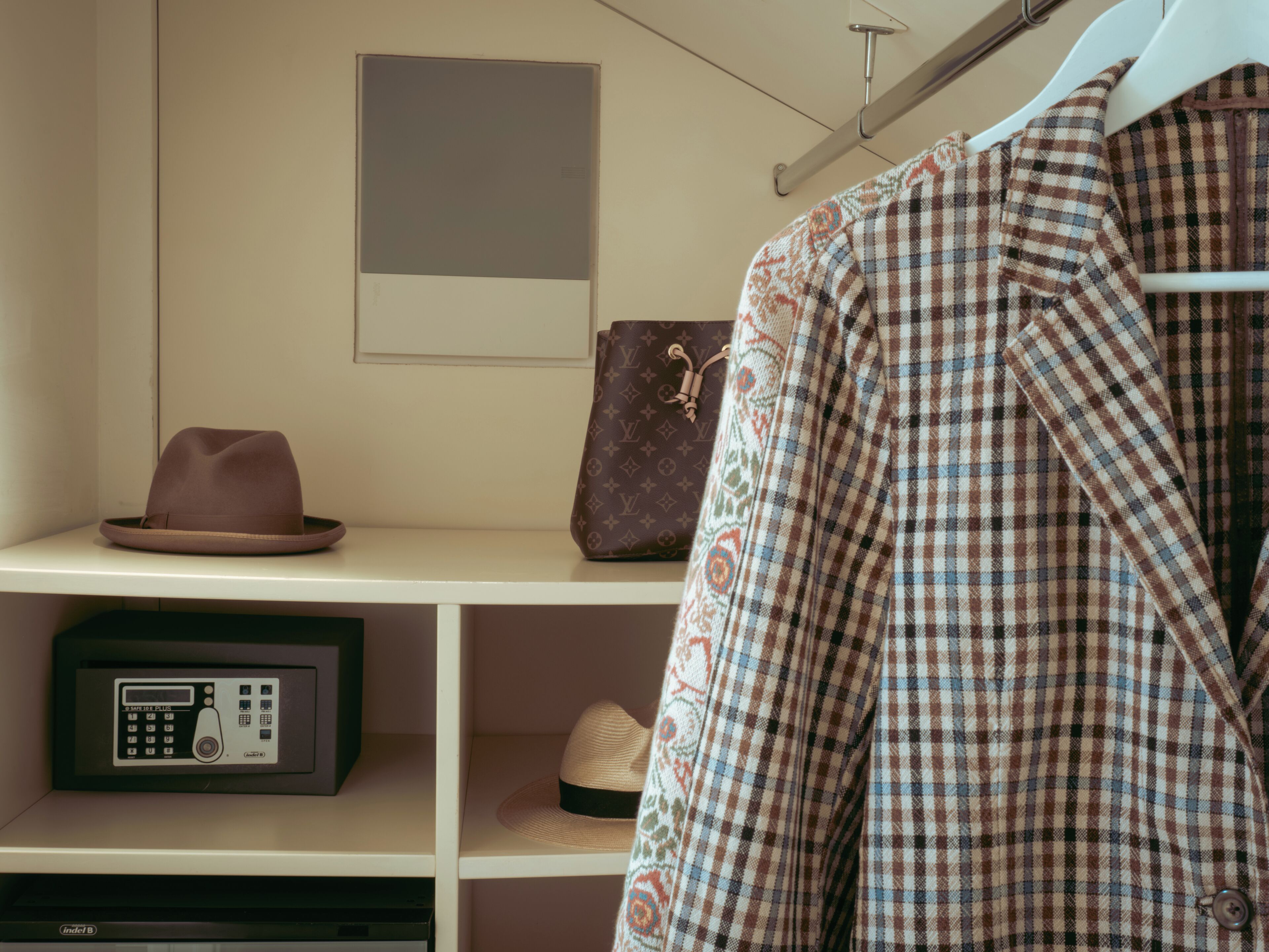 Un armadio con una rastrelliera, un cappello, una giacca fantasia e una borsa Louis Vuitton.
