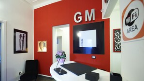 A reception desk with a red wall, a large screen, and a 'WiFi Area' sign. - Gran Maestro B&B (Palermo)