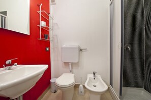 A bathroom with a white sink, toilet, bidet, and a shower with black tiled walls. - Gran Maestro B&B (Palermo)