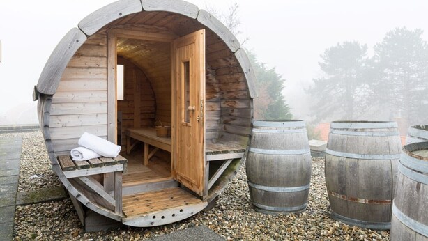 Un sauna rustique en bois, doté d’un banc et d’une serviette, entouré de grandes cuves.