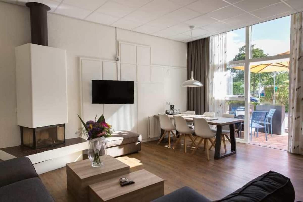 Uma sala de estar moderna com lareira, uma área de jantar com mesa e cadeiras, e uma grande janela com cortinas.