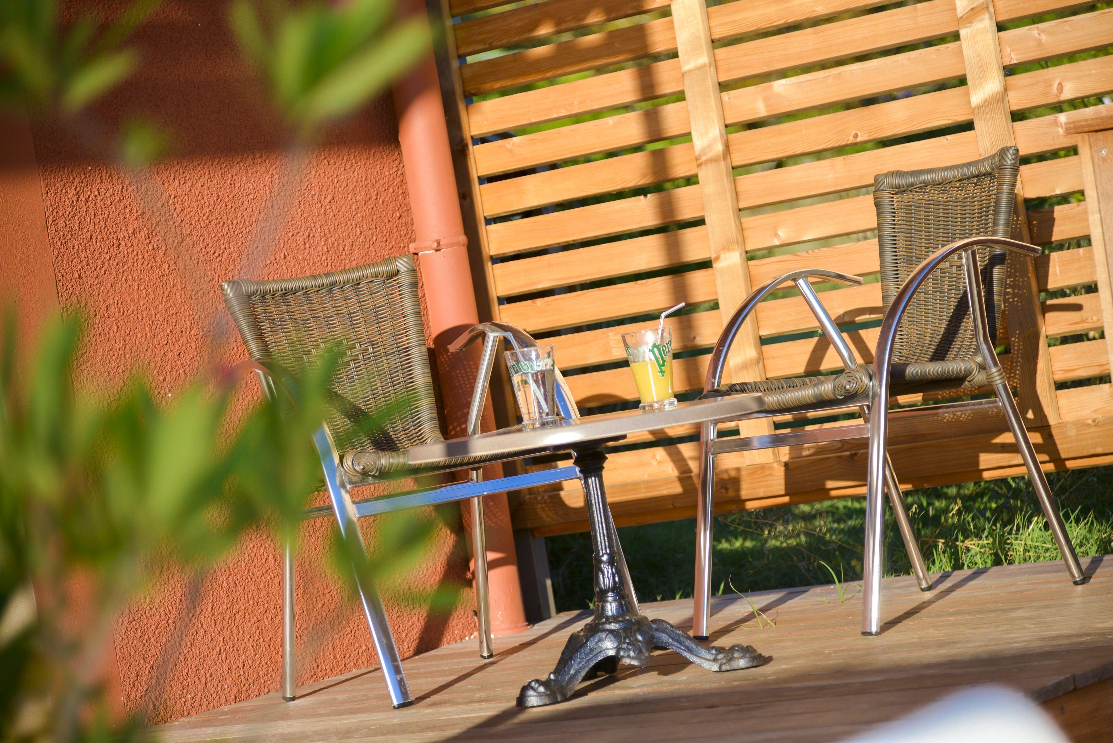 A wooden table with metal chairs, a glass with a straw, and a yellow cup on it.
